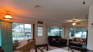 A cozy living room with a dining table, chairs, a sofa, and a large window offering a view of the outdoors. - Cozy canal front home. Minutes from Sebring International Raceway. (Lake Placid)