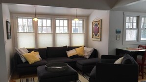 A living room with a sectional sofa, a coffee table, and a dining area with a table and chairs. - Apartment in the heart of Leland, just a short walk to Fishtown. (Leland)