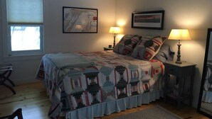 A bedroom with a bed, two bedside lamps, a window, and two framed pictures on the wall. - Apartment in the heart of Leland, just a short walk to Fishtown. (Leland)