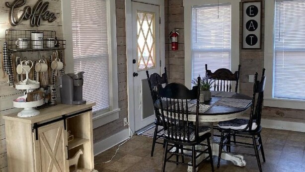 Un comedor con una mesa y sillas de madera, una encimera de cocina con equipo para hacer café, y un cartel en la pared que dice "Coffee".