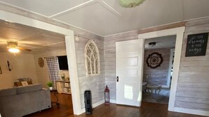 Una habitación amplia con suelo de madera, una puerta blanca y un ventanal decorativo.