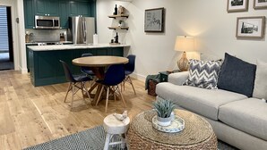 A modern kitchen with teal cabinets, a dining area with a round table and blue chairs, a living room with a beige sofa and a lamp, and a wooden floor. - Rosies place (Kimberling City)