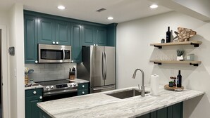 A modern kitchen with teal cabinets, stainless steel appliances, a marble countertop, and built-in shelves with decorative items. - Rosies place (Kimberling City)