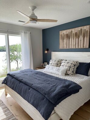 A bedroom with a bed, a ceiling fan, a view of the outdoors, and a wall-mounted light.