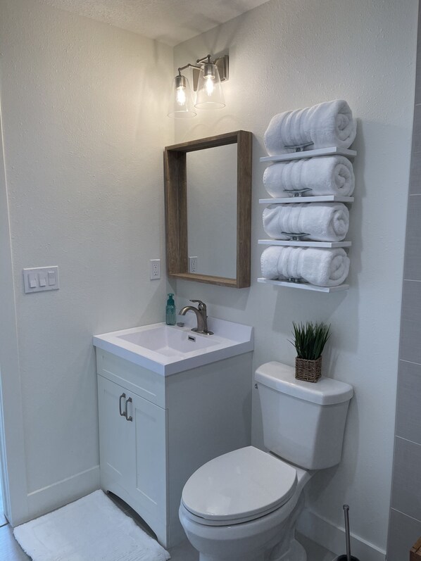 A bathroom with a white sink, a mirror, a toilet, and a towel rack with neatly folded towels.