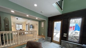 Un ampio soggiorno con soffitto alto, una scala in legno e vista su un paesaggio innevato.