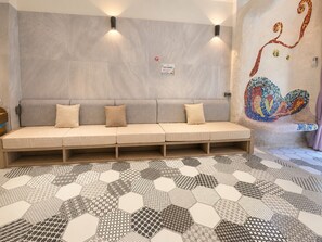 A room with a sofa, hexagonal patterned floor, wall-mounted light fixtures, and a mosaic artwork. - Dory Hostel  (Liuqiu)