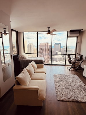 Un salon moderne avec une grande fenêtre, un canapé, un tapis et un ventilateur de plafond.
