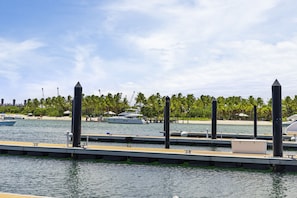 Una marina con barcos amarrados, una playa de arena y palmeras al fondo.