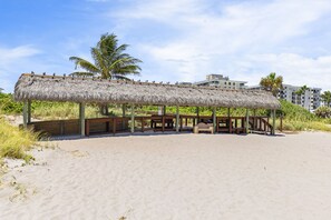 Una estructura frente al mar con techo de paja, bancos de madera y una playa arenosa.