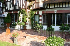 Un edificio tradicional con entramado de madera y un patio de ladrillo, plantas en macetas y asientos al aire libre.