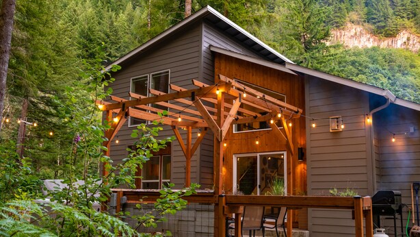 A cabin with a wooden deck, string lights, and a grill area.