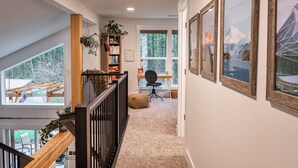 A hallway with a wooden staircase, a bookshelf, a desk with a chair, and framed pictures on the wall.