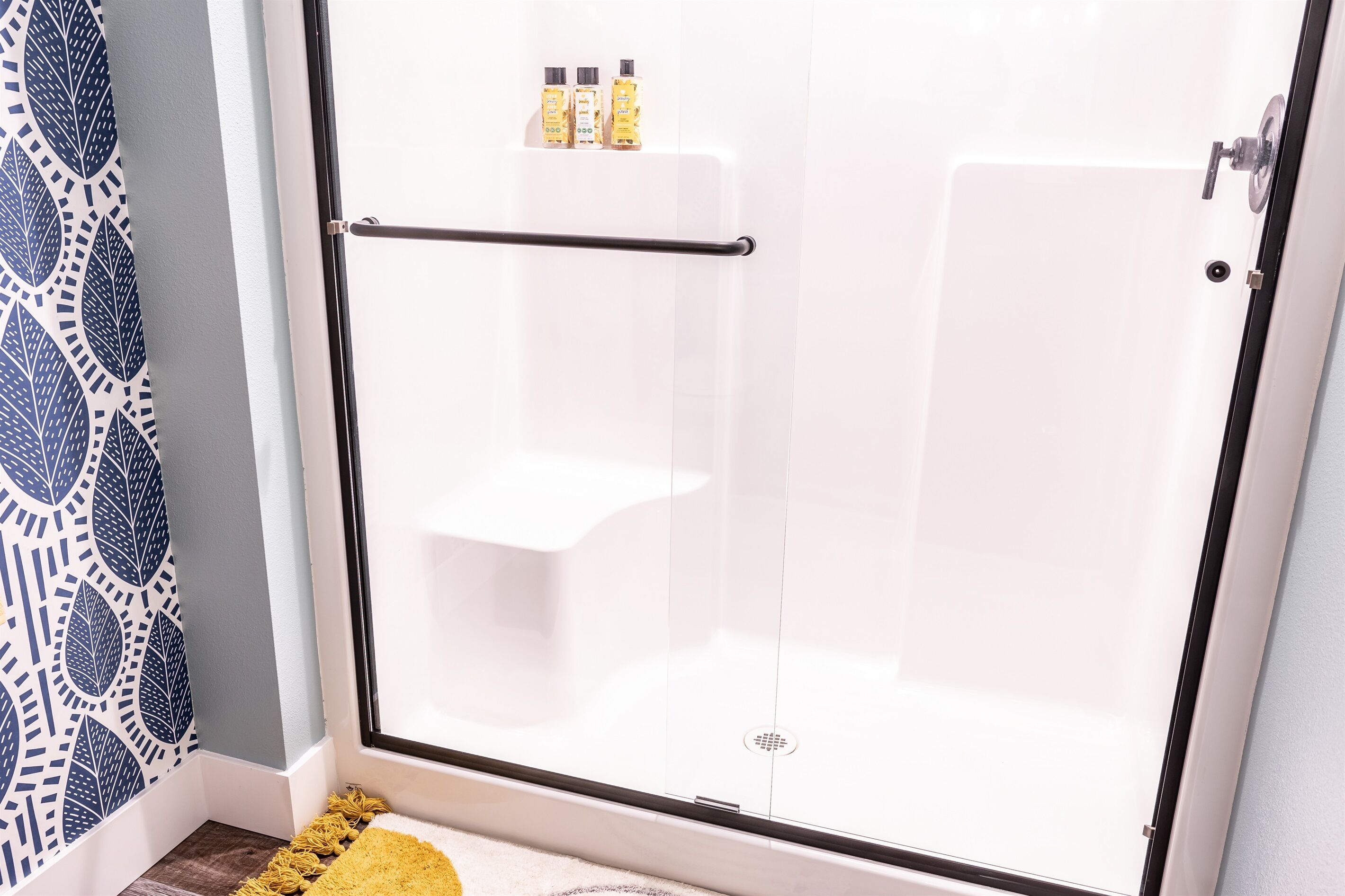 A glass-enclosed shower area with a black towel rack and two bottles of shampoo on the wall.