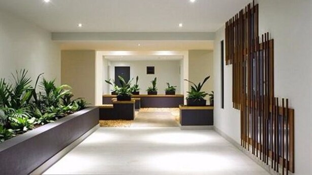 A modern interior with a reception desk, potted plants, and a decorative wooden panel on the wall. - Essence Apartments Chermside (Brisbane)