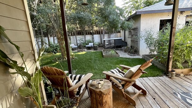 A covered patio with wooden flooring, two wooden chairs with striped cushions, a small wooden table, and potted plants. - Downtown Eclectic Bungalow (Oakdale)