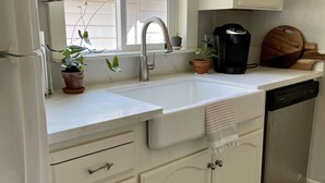 A kitchen with white cabinets, a double sink, a coffee maker, and a potted plant. - Downtown Eclectic Bungalow (Oakdale)