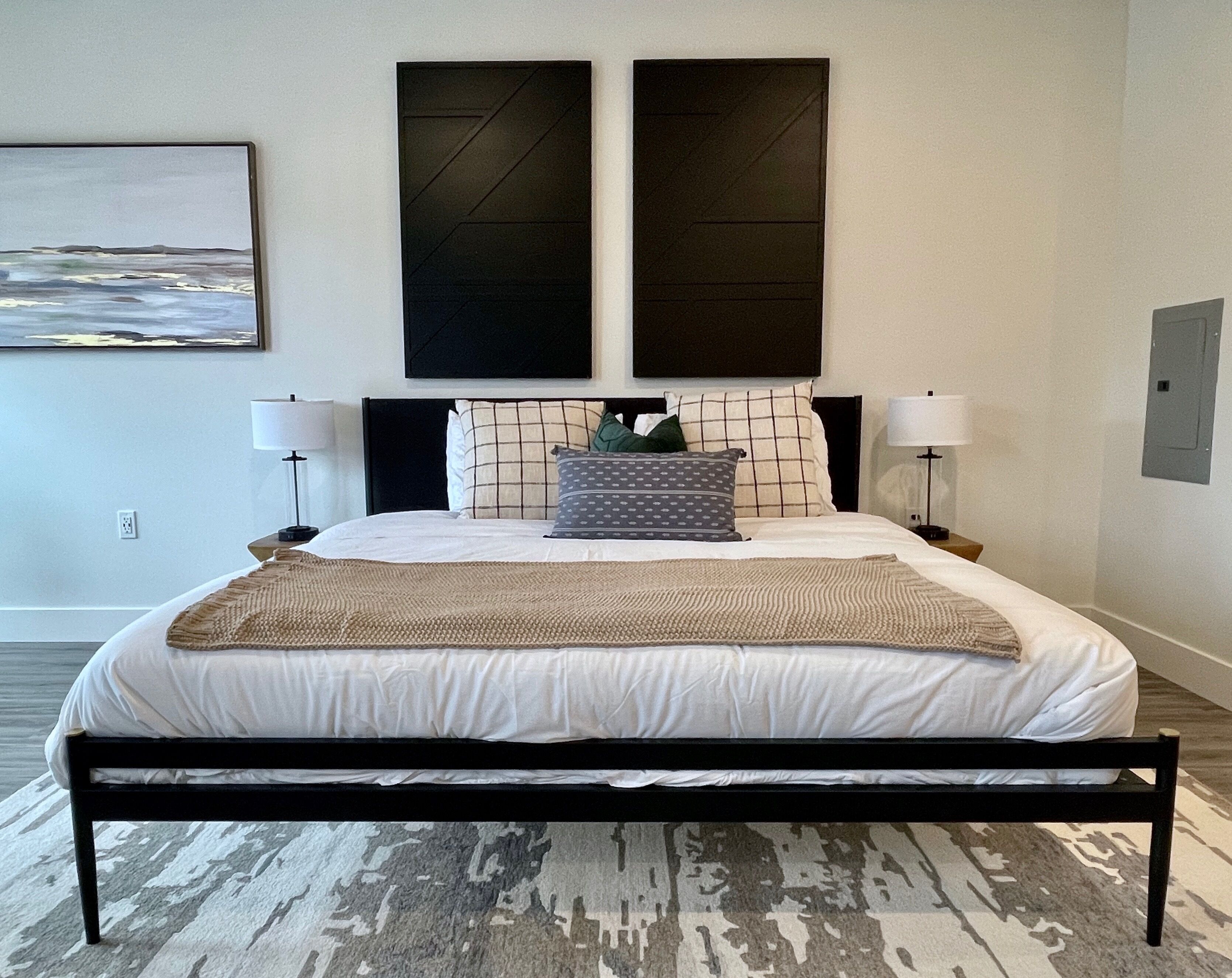 A modern bedroom with a large bed, two nightstands, a wall-mounted TV, and a painting on the wall.