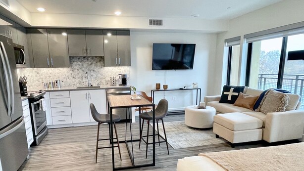 A modern kitchen with a dining area, a flat-screen TV, and a living area with a sofa and ottoman. - Rooftop Hot Tub in Downtown Walnut Creek (Walnut Creek)