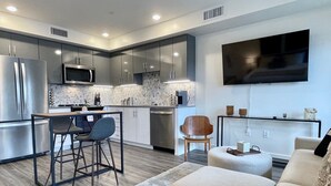 A modern kitchen with stainless steel appliances, a dining area with a bar stool, and a living area with a sofa and a flat-screen TV. - Rooftop Hot Tub in Downtown Walnut Creek (Walnut Creek)