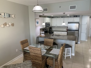 Una cocina moderna con armarios blancos, un refrigerador de acero inoxidable y un comedor con sillas de mimbre y una mesa de vidrio.