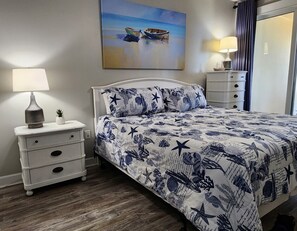 Une chambre à coucher avec un lit, une table de chevet, une lampe et un tableau représentant des bateaux accroché au mur.