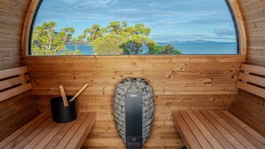 Una sauna con bancos de madera, pared de piedra y vistas a árboles y agua.