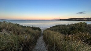 Un sentier sablonneux qui mène à une plage bordée de dunes herbeuses de chaque côté.