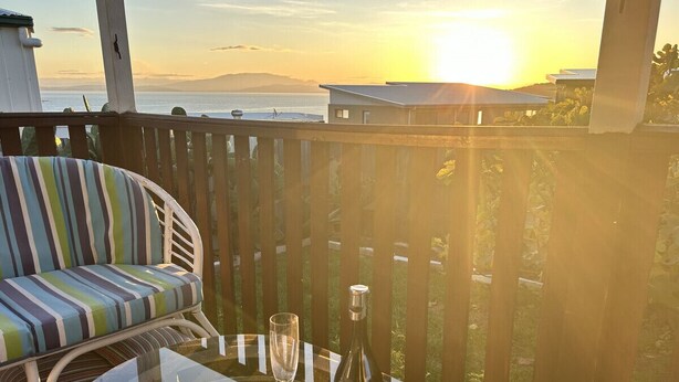 Un balcon avec un canapé à rayures et une table sur laquelle se trouvent une bouteille de vin et un verre.