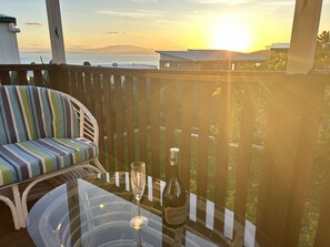 Un balcone con un divano a righe, un tavolo con una bottiglia di vino e un bicchiere.