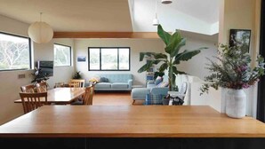 A spacious living area with a wooden dining table, a blue sofa, and a large plant. - Beachside Family Surf Retreat (Carlton)