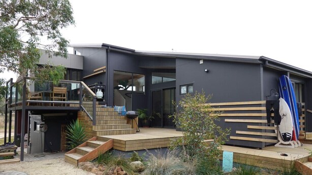 A modern house with a wooden deck, a staircase, and a surfboard. - Beachside Family Surf Retreat (Carlton)
