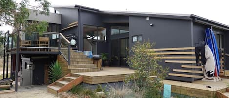 Une maison moderne dotée d’une terrasse en bois, d’un escalier et d’une planche de surf.