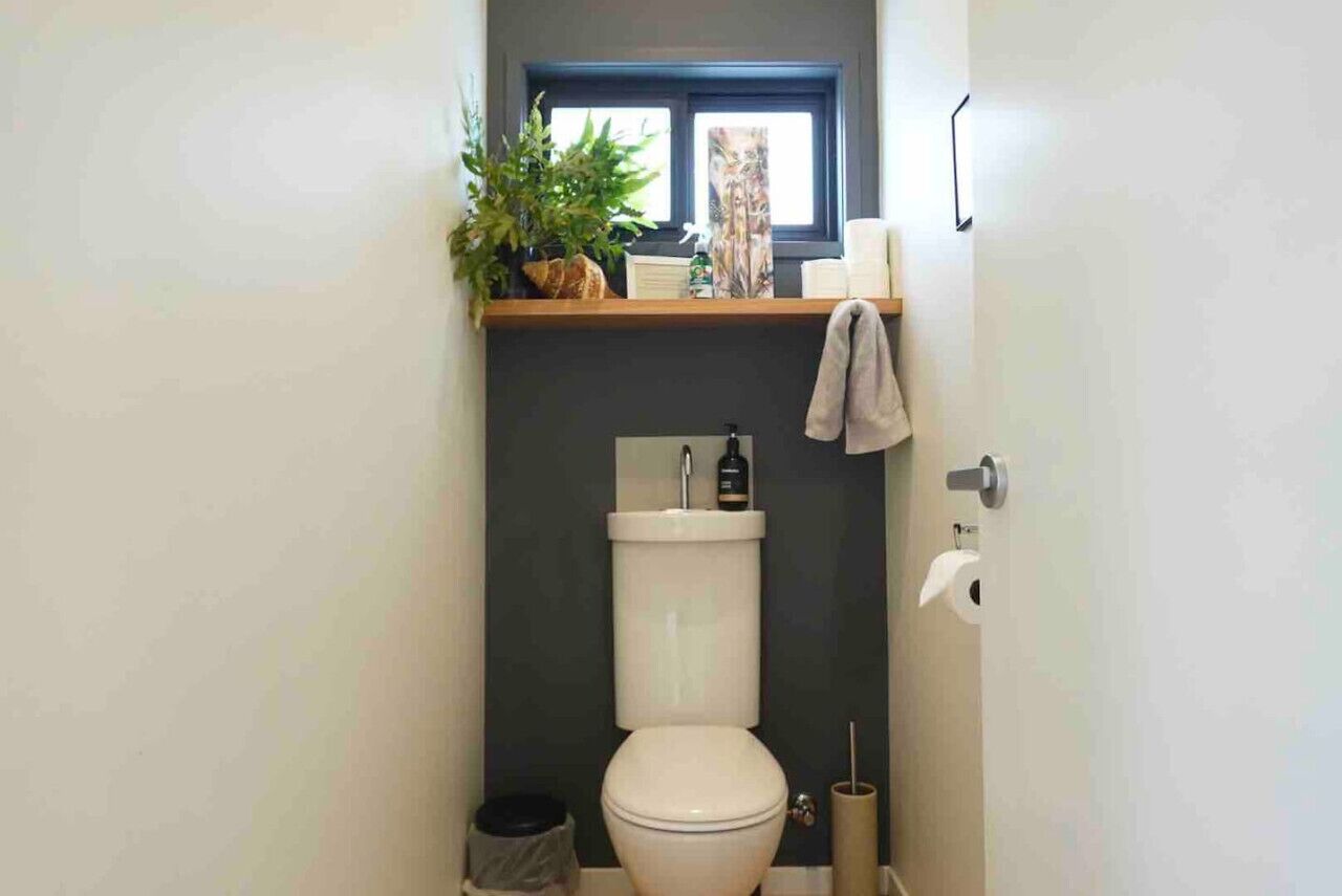 Une petite salle de bain comprenant des toilettes, une étagère avec une plante et une fenêtre située au-dessus des toilettes.