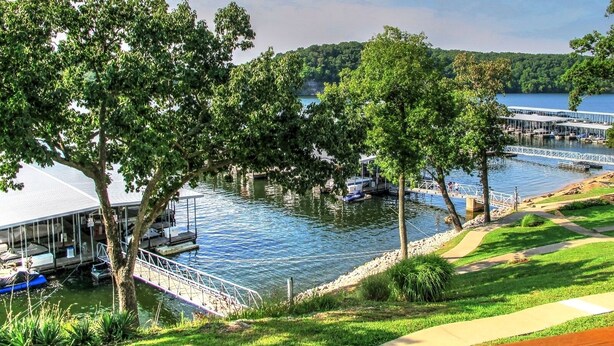 Vista de un lago con un muelle, barcos y una zona cubierta con asientos.