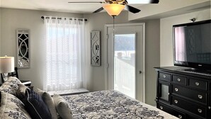 Un dormitorio con cama, ventilador de techo, televisor, cómoda y ventana con cortinas.