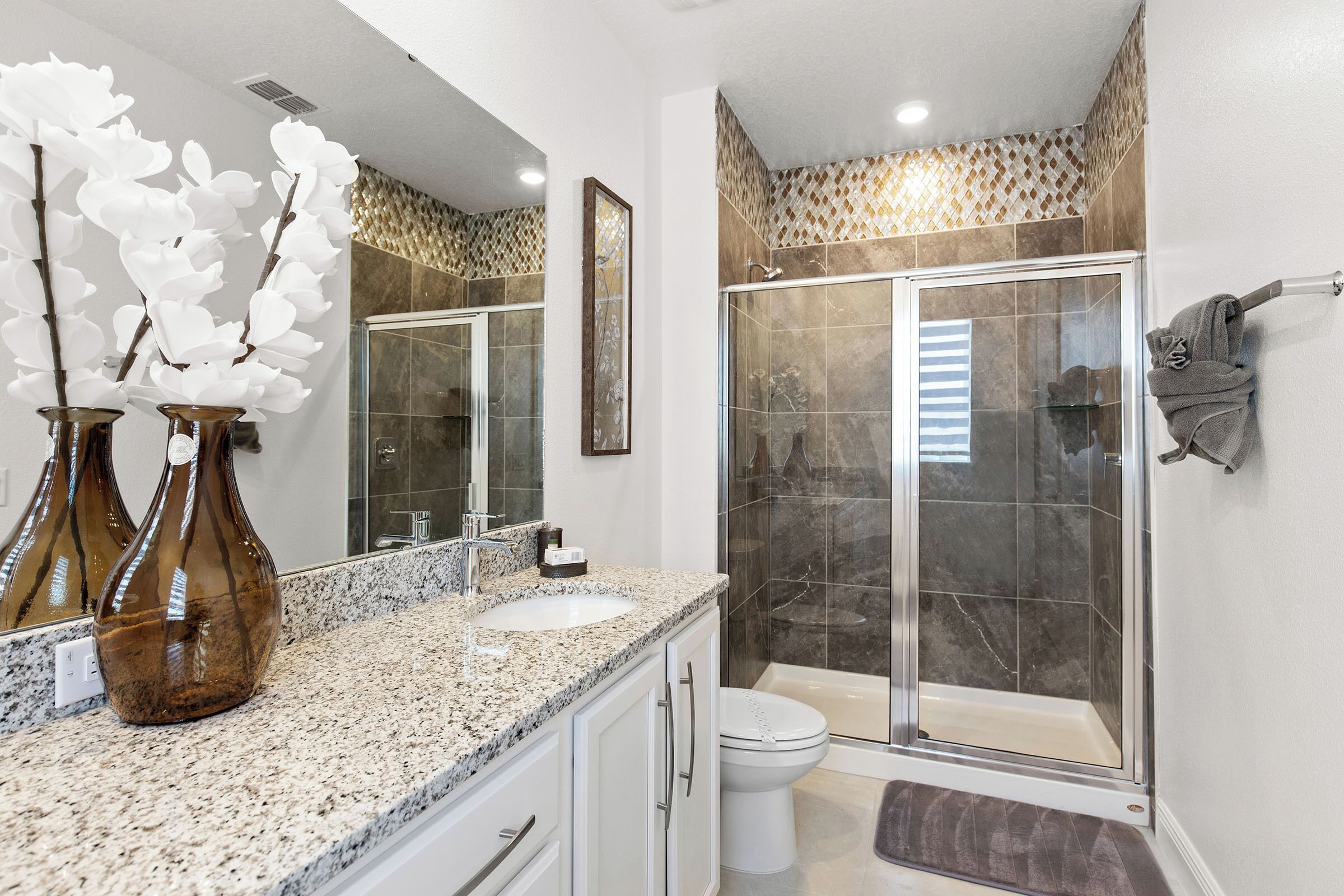 Une salle de bain dotée d’un comptoir en granit, d’un lavabo blanc et d’une cabine de douche en verre.