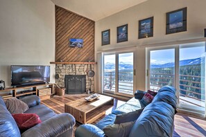 A modern living room with a stone fireplace, leather sofas, a wooden coffee table, and large windows offering mountain views.