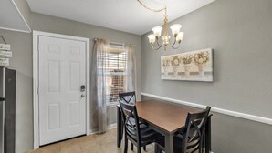 A dining area with a wooden table and chairs, a chandelier, a white door, and a window with blinds. - Downtown Frisco Gem (Frisco)