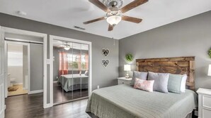 A bedroom with a large bed, a ceiling fan, a nightstand with a lamp, and a view through a glass door to another room. - Downtown Frisco Gem (Frisco)