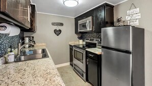 A modern kitchen with stainless steel appliances, a granite countertop, and a heart-shaped sign on the wall. - Downtown Frisco Gem (Frisco)