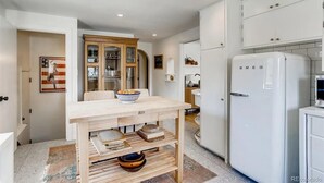 Eine kleine Küche mit einem Holztisch, einem weißen Kühlschrank und einem Schrank mit Glastüren.