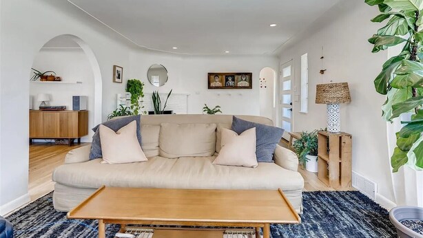 Ein Wohnzimmer mit einem beigefarbenen Sofa, einem Holztisch und einer großen Pflanze.