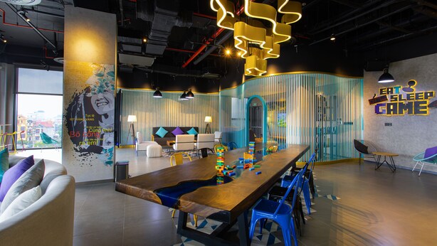 A modern lounge area with a long wooden table, blue chairs, and a colorful wall mural. - Tru by Hilton Lang Son City Centre (Dong Kinh)