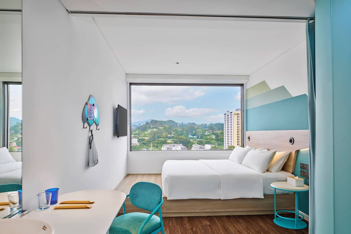 A modern hotel room with a large window, a bed, a desk, and a chair.