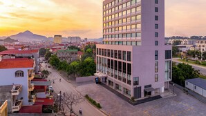 A modern building with a prominent sign, surrounded by a mix of residential and commercial buildings, set against a sunset sky. - Tru by Hilton Lang Son City Centre (Dong Kinh)