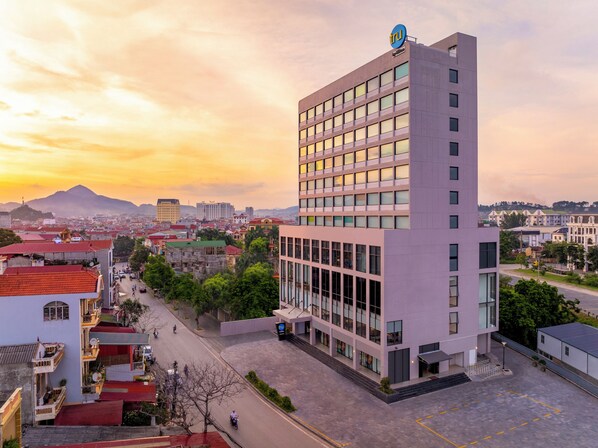 A modern building with a prominent sign, surrounded by a mix of residential and commercial buildings, set against a sunset sky.