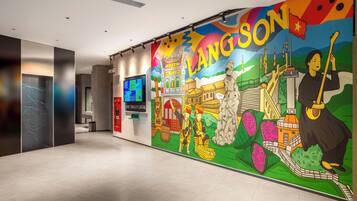 A modern hotel lobby with a colorful mural depicting local culture, a digital information board, and a traditional Vietnamese instrument.