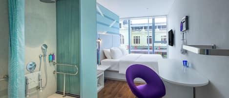 Un hotel moderno con ducha, cama, escritorio pequeño y vistas a la ciudad.