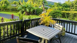 A wooden deck with a table and chairs, overlooking a lush garden and a body of water. - Inave Oasis Villa ‘ Your home away from Home’ (Arorangi)
